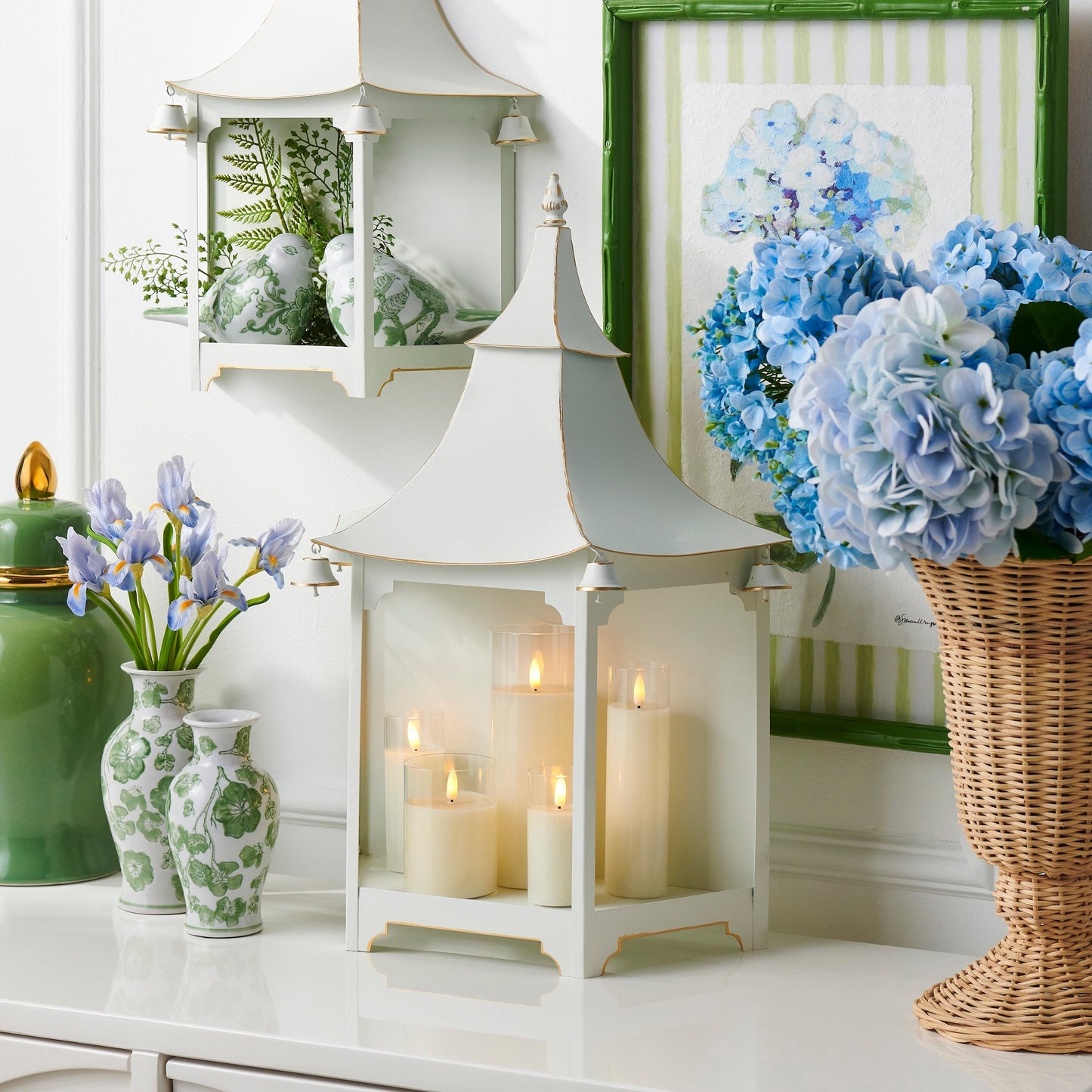 Decorative setting with white pagoda lanterns, candles, floral arrangements, and vases on a white surface.