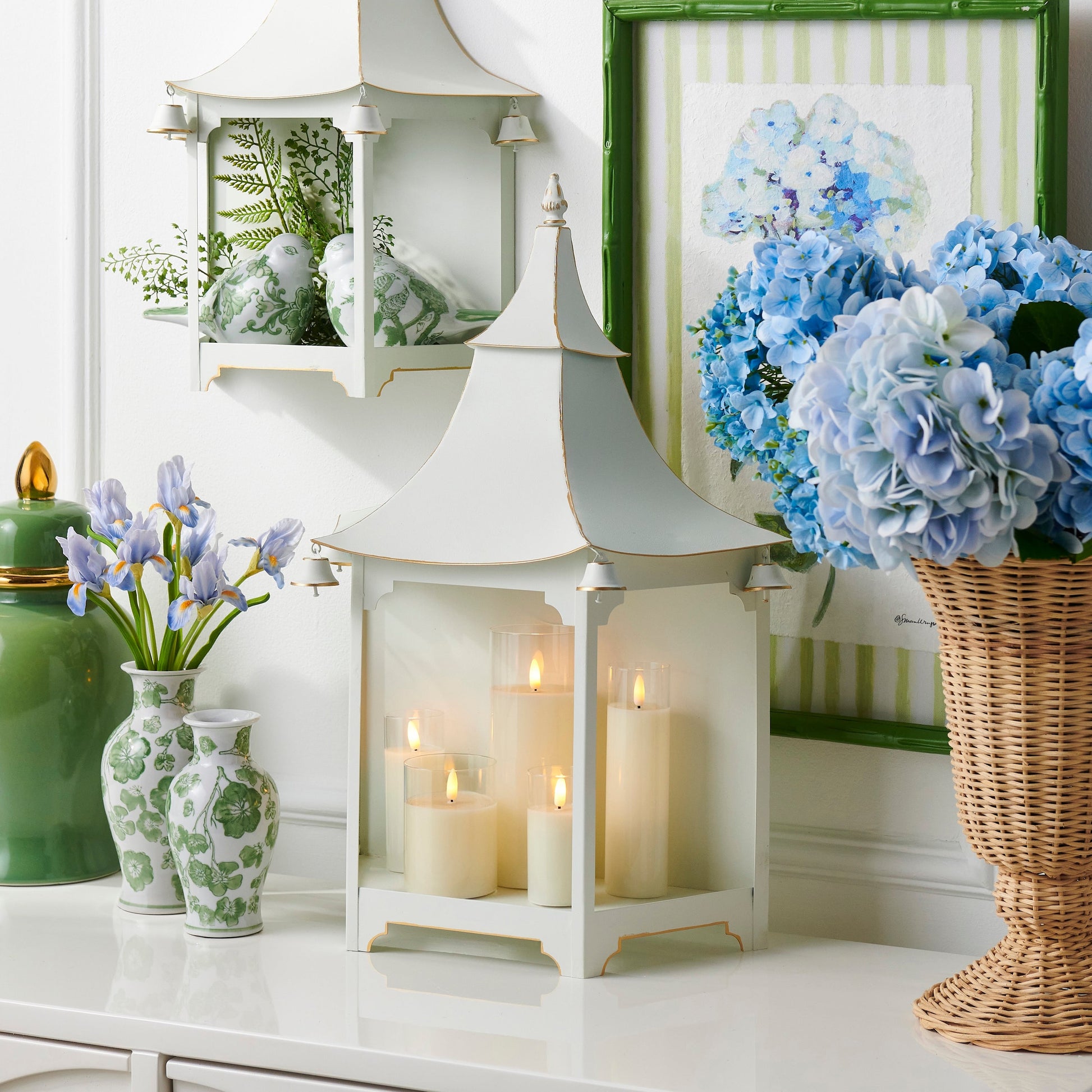 Decorative setting with white pagoda lanterns, candles, floral arrangements, and vases on a white surface.