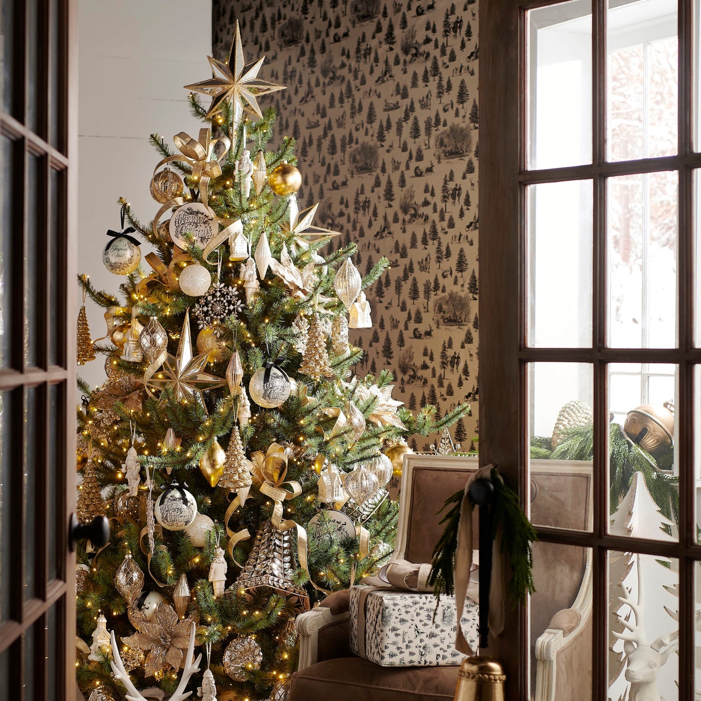 Decorated Christmas tree in a room with patterned wallpaper and a chair.