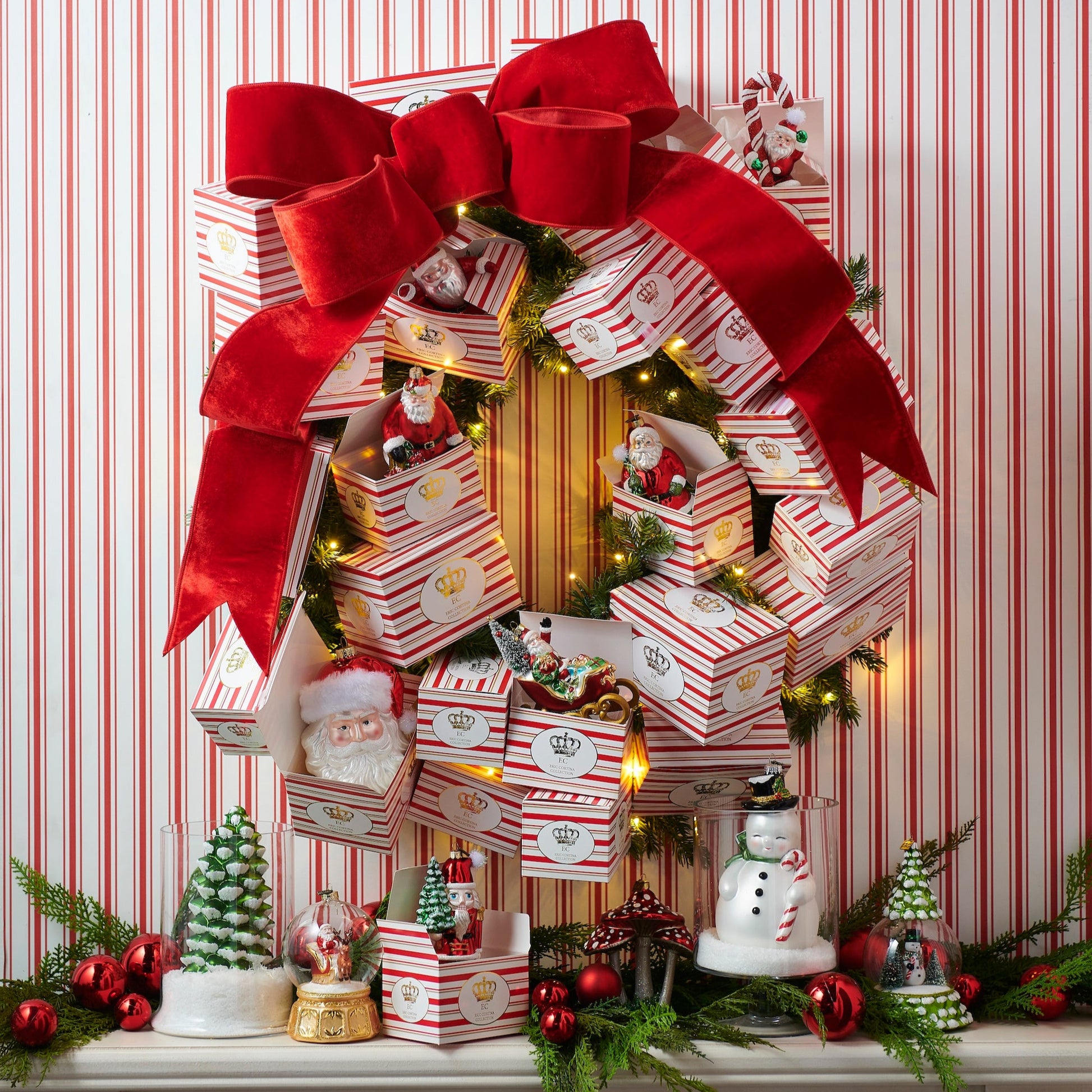 Decorative Christmas scene with stacked gift boxes, Santa Claus figurines, and festive decorations against a striped red and white background.