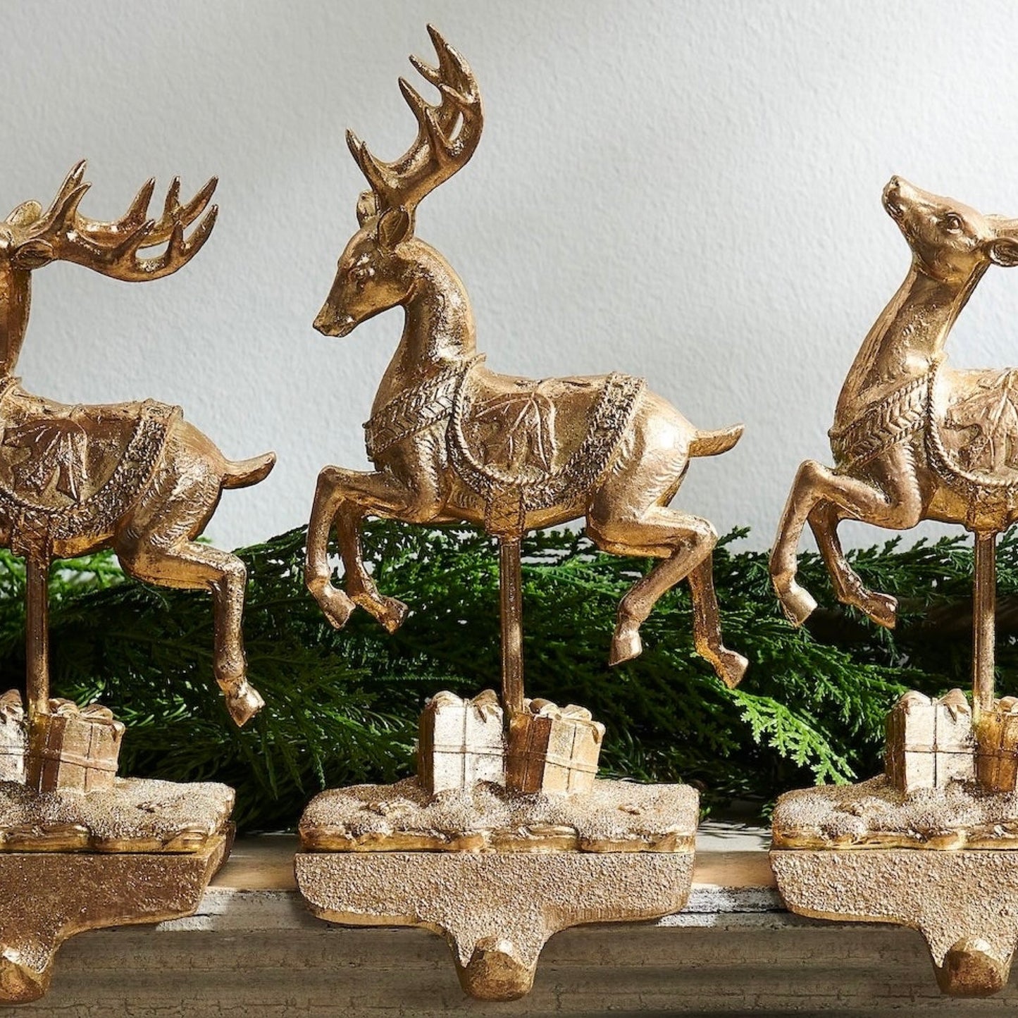 Three gold deer figurines on a decorative base with a Christmas tree in the background.
