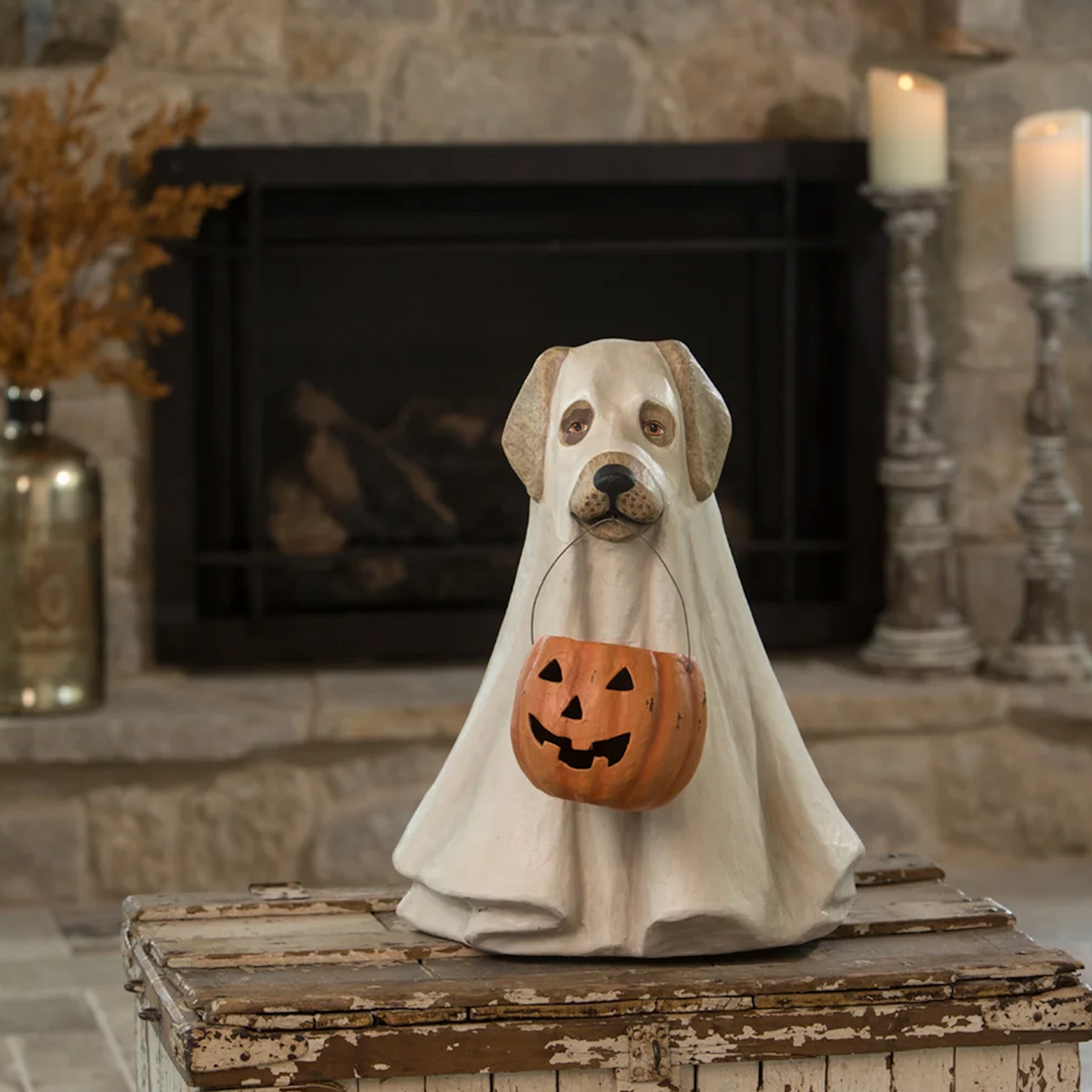 Decorative Halloween dog figurine in a ghost costume with a pumpkin basket in front of a stone fireplace.