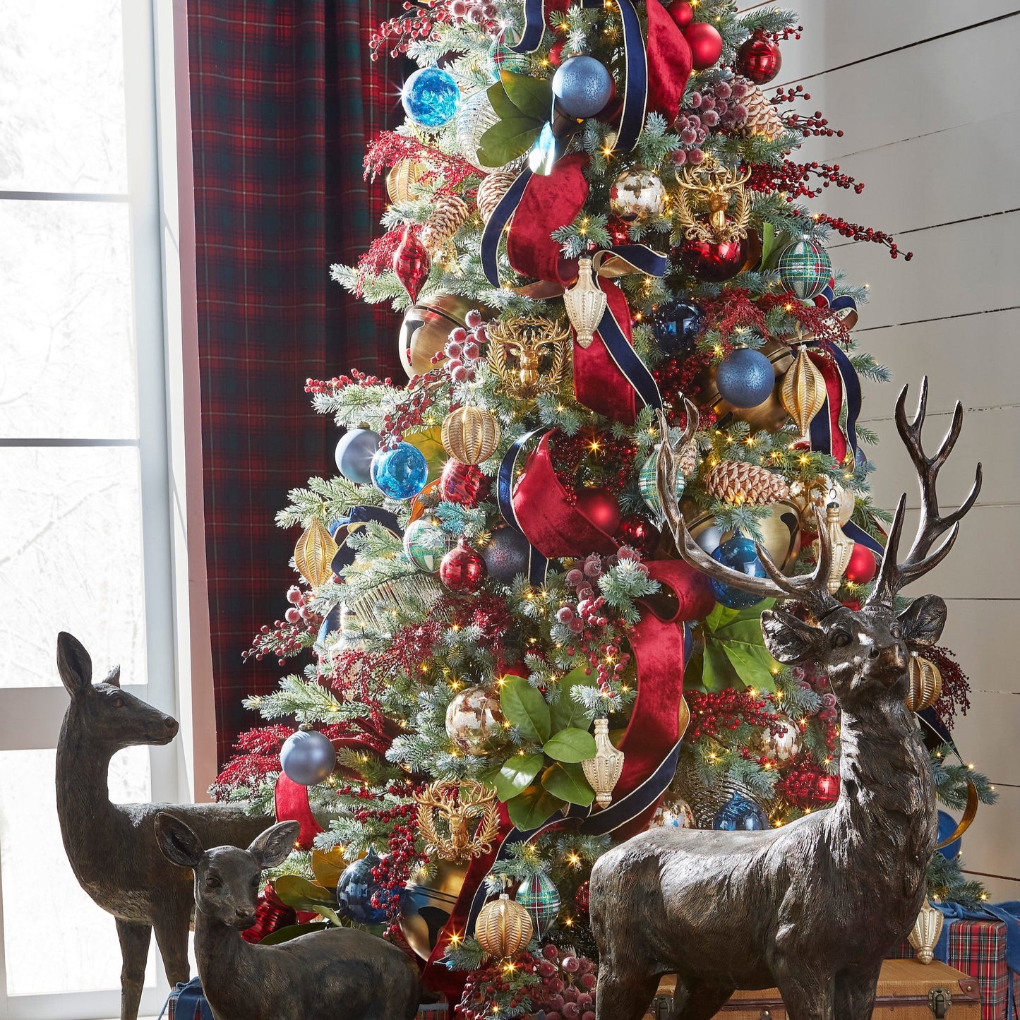 Decorated Christmas tree with ornaments and ribbons, flanked by deer statues.