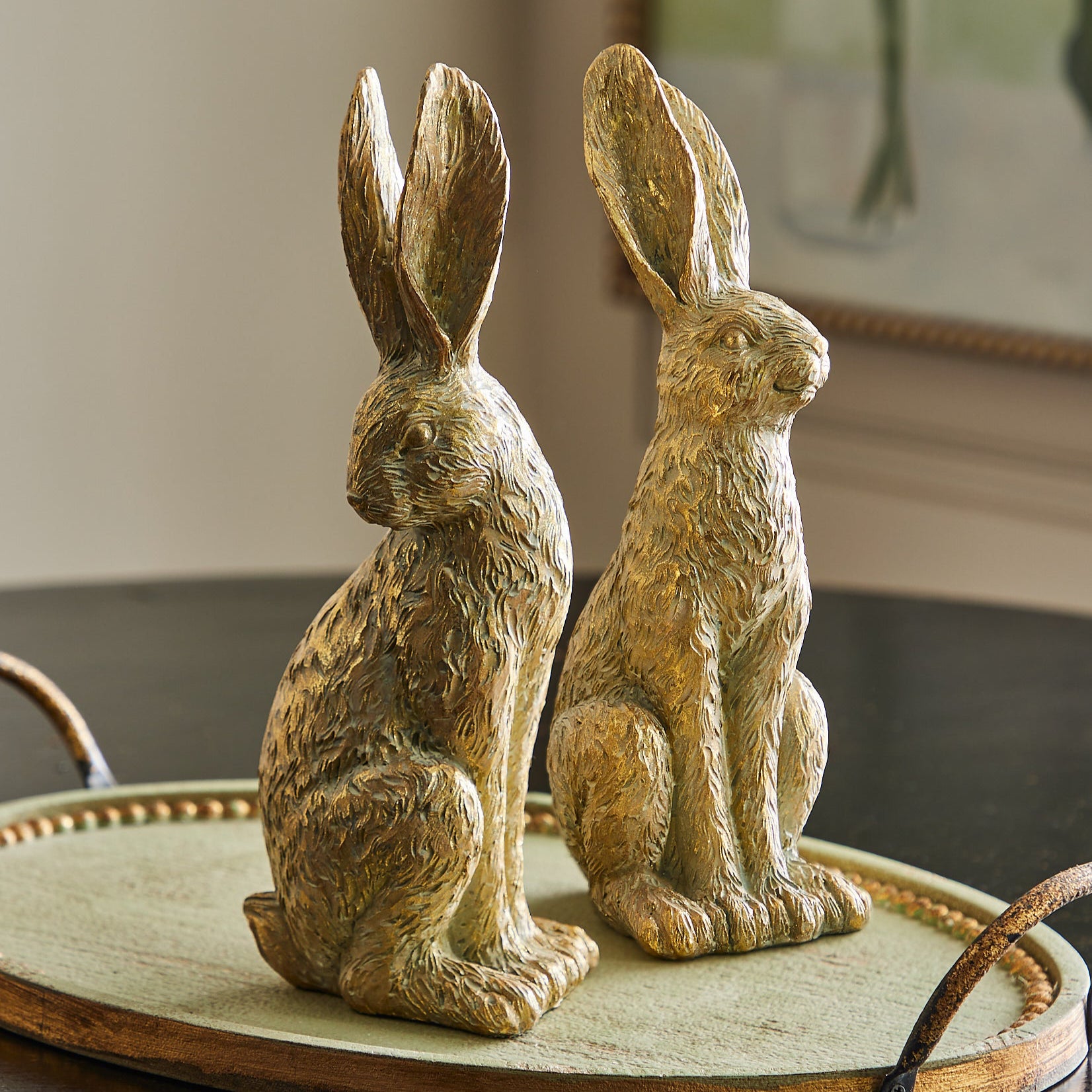 Two gilded gold leaf rabbits with a soft gold finish, sitting on a surface, likely a part of Easter decor.
