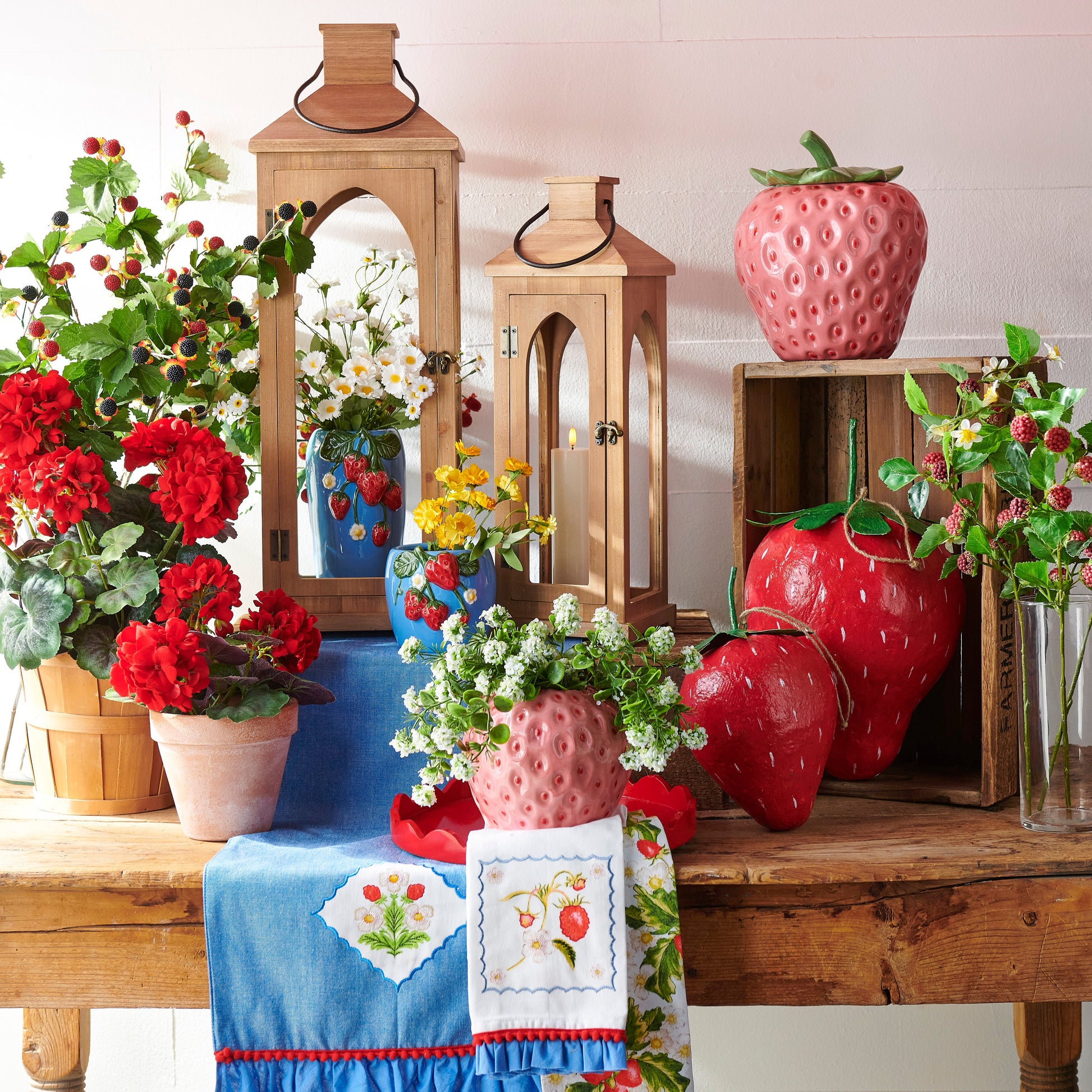 Decorative setting with red and white striped awning, wooden lanterns, strawberry-themed vases, and floral arrangements on a table.