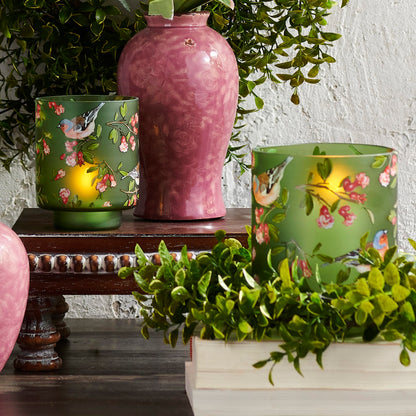 Decorative vases with floral and bird patterns on a table with greenery.