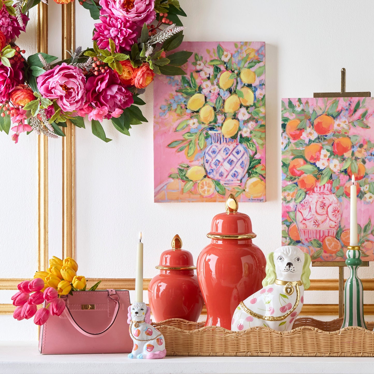 Decorative items including vases, a handbag, and floral arrangements on a table with a white wall and gold frame in the background.