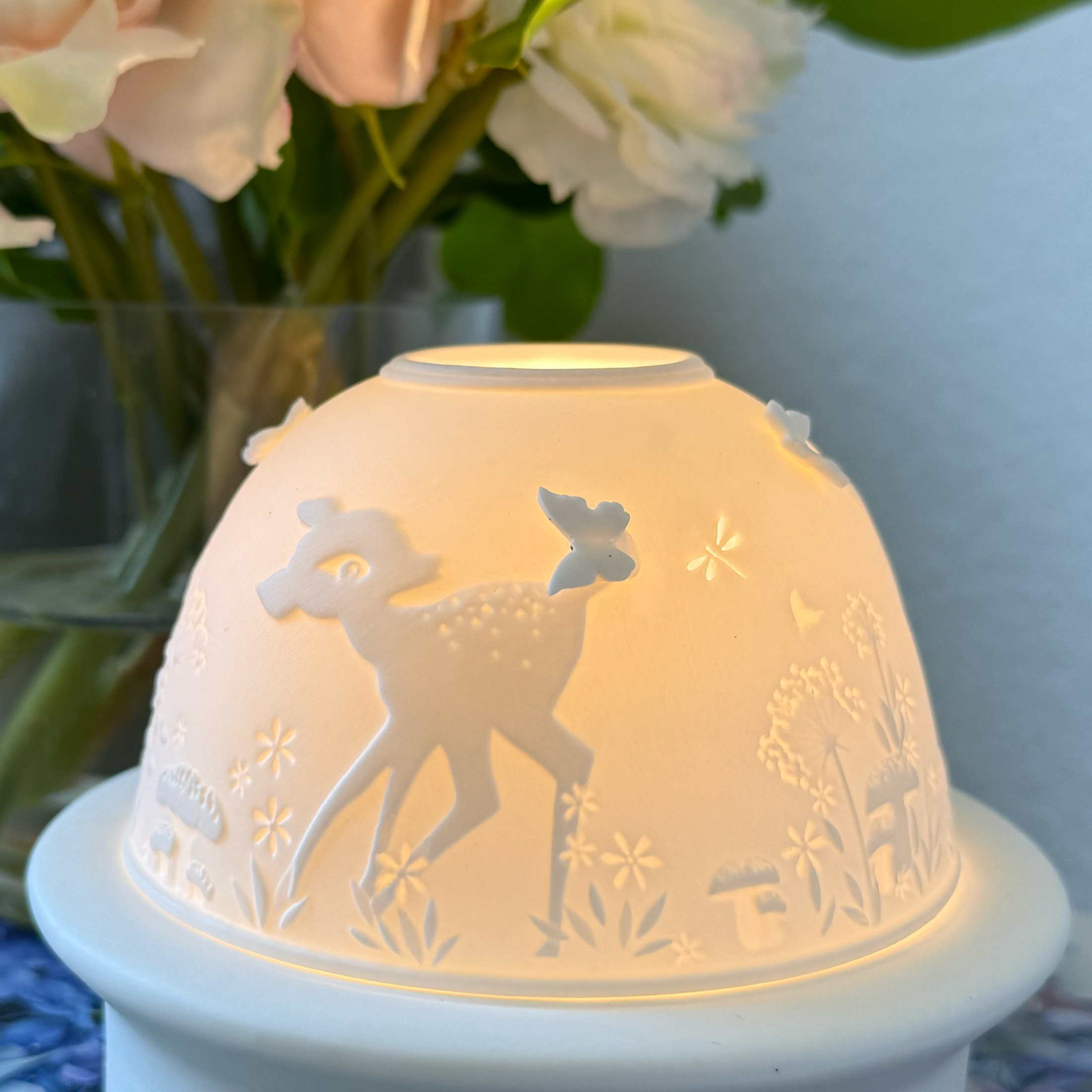 A white porcelain dome votive light with a baby fawn and butterfly design, sitting on a tray.